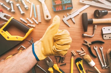 A man's thumbs up in front of an array of handyman tools on table